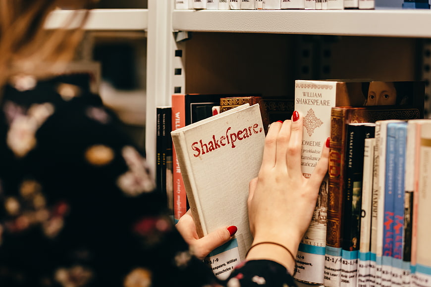 Woman selecting Shakespeare book from library shelf