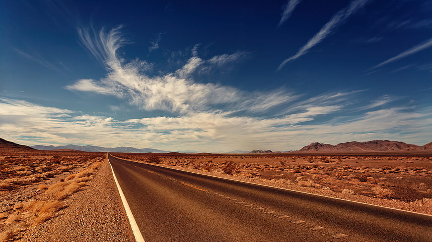 Endless Desert Highway Stretching Toward Distant Mountains Under Blue Sky