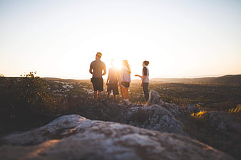 Group of friends hiking on rocky hilltop at sunset