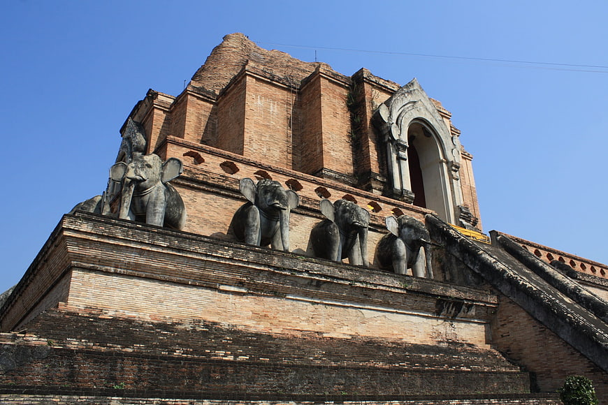 Ancient brick temple with elephant statues against blue sky