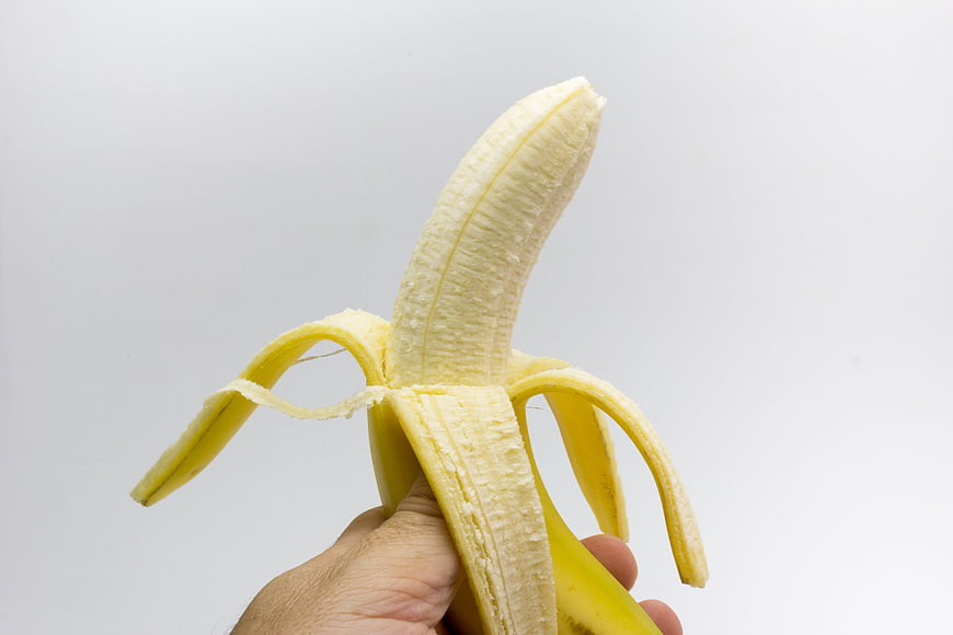 Hand Holding Half-Peeled Yellow Banana Against White Background