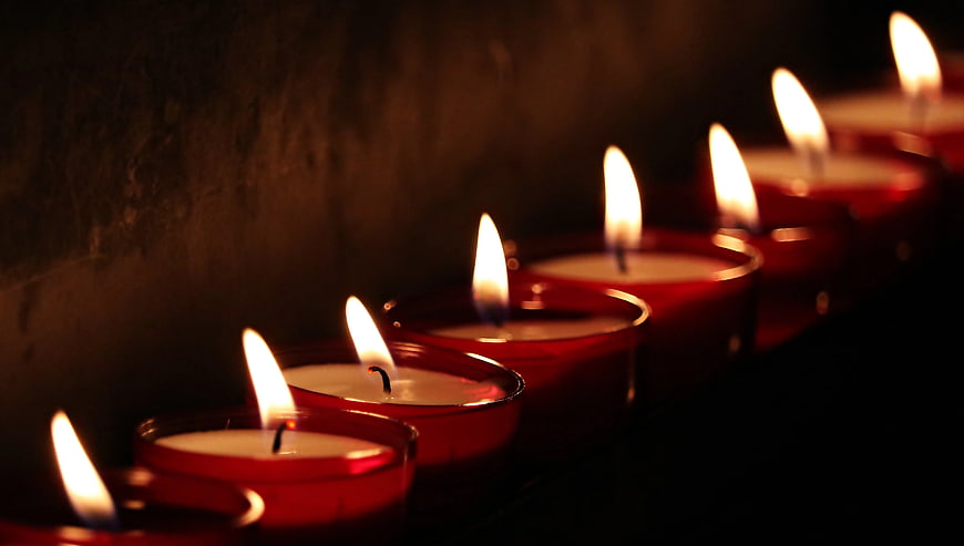 Row of lit red votive candles in dark setting