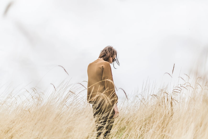 Man in brown sweater standing in tall dry grass field