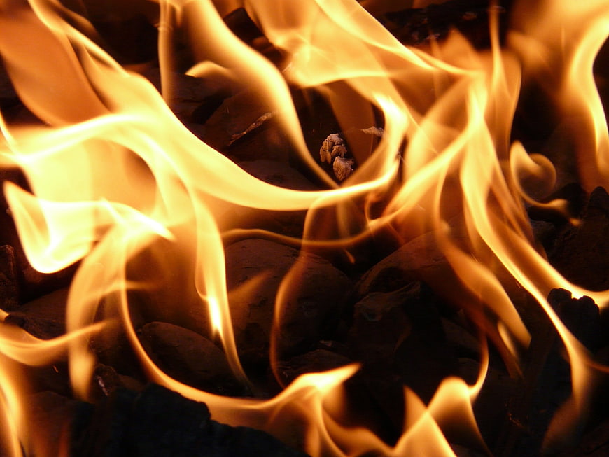Close-up of bright orange flames burning over dark charcoal