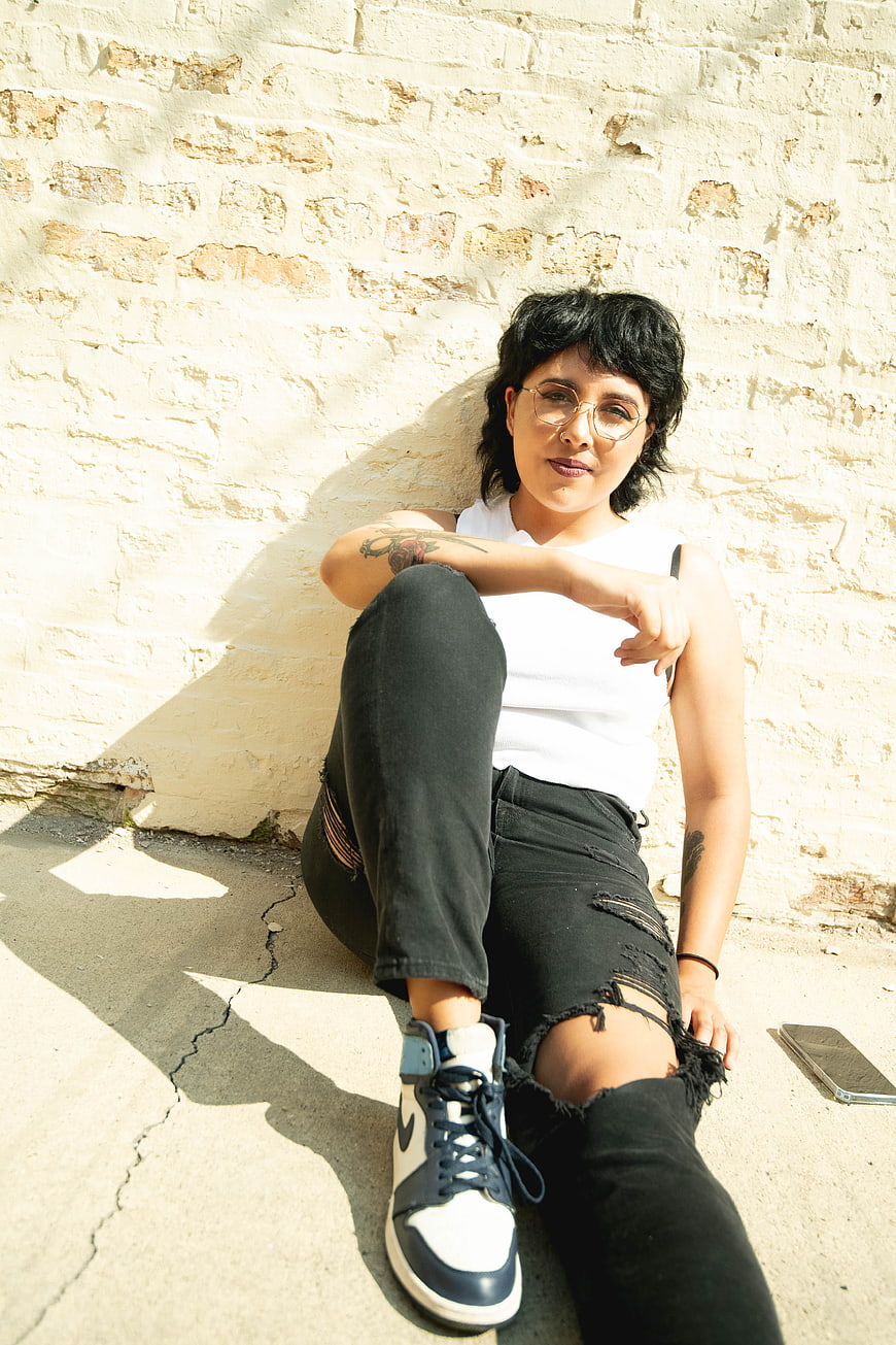 Stylish Woman Sitting Against White Brick Wall in Sunlight