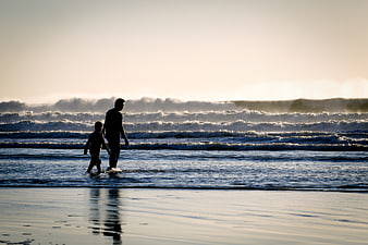 Silhouette of Father and Son Walking on Beach at Sunset