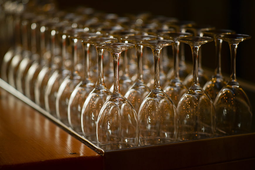 Rows of empty wine glasses on a wooden bar counter