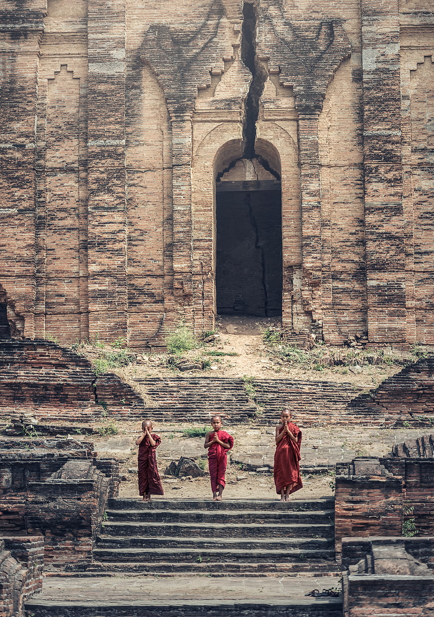 Three young Buddhist monks praying at ancient temple ruins