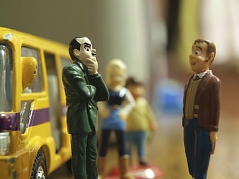 Miniature toy figures of men and children standing near a yellow toy bus