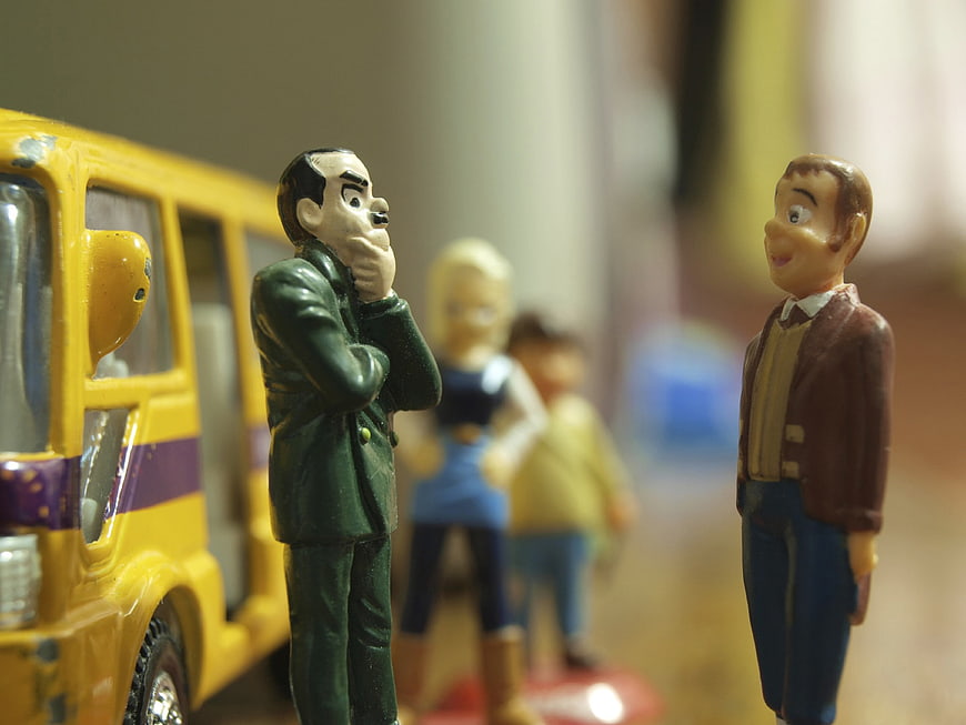 Miniature toy figures of men and children standing near a yellow toy bus