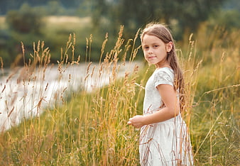 Young girl in white dress standing in tall summer grass