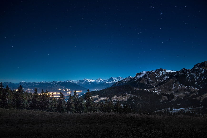 Starry Night Sky Over Snow-Capped Mountains and Lake