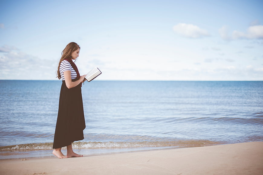 Woman Reading Book on Sandy Beach by Ocean
