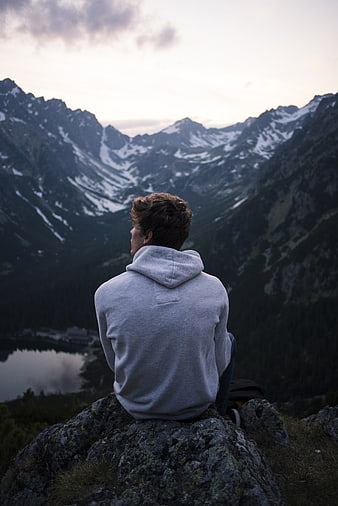 Man sitting on rock overlooking snowy mountain valley at dusk