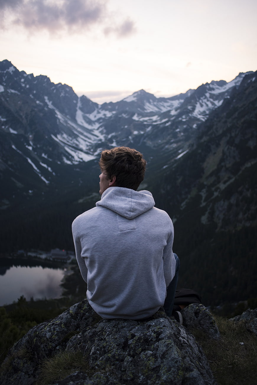 Man sitting on rock overlooking snowy mountain valley at dusk