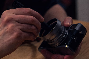 Close-up of hands cleaning camera lens with blower