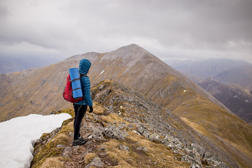 Hiker with backpack standing on mountain ridge overlooking peaks