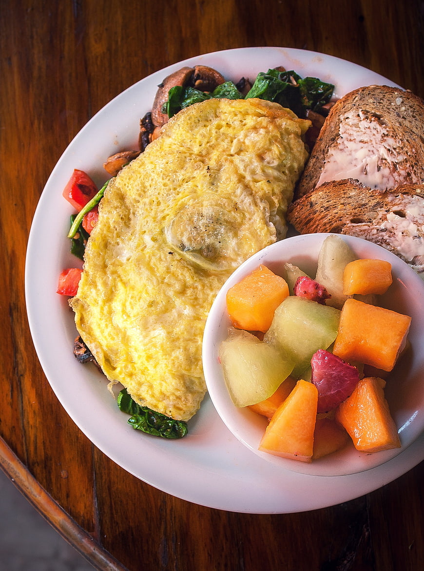 Healthy Breakfast Plate With Omelet, Spinach, Toast, And Fresh Fruit Bowl