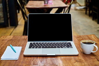 Laptop with black screen, coffee cup, and notebook on wooden table