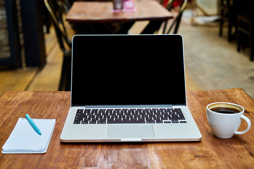 Laptop with black screen, coffee cup, and notebook on wooden table