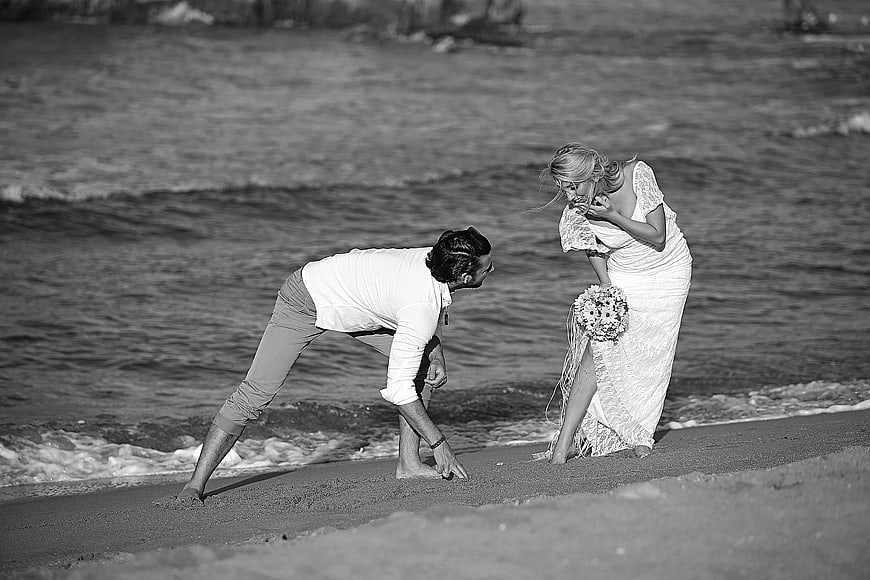 Playful wedding couple laughing on sandy beach shoreline