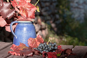 Blue ceramic pitcher with red grape leaves and grapes on wooden table