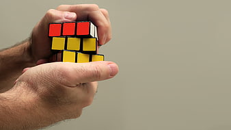 Hands holding a Rubik's Cube puzzle against a gray background