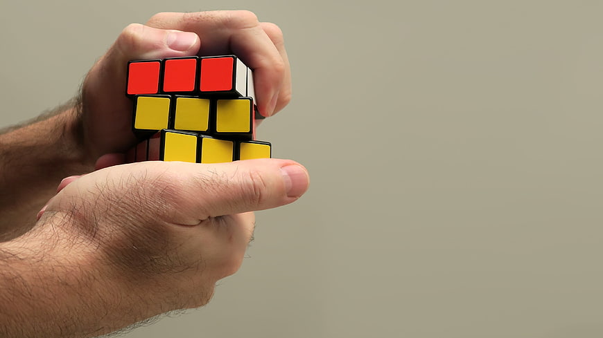 Hands holding a Rubik's Cube puzzle against a gray background