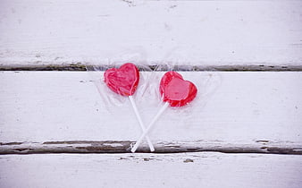 Two red heart-shaped lollipops on a rustic white wooden surface