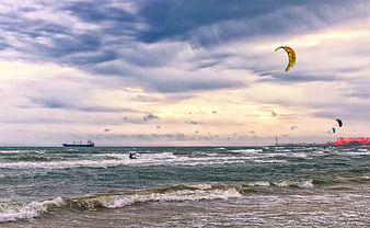 Kitesurfer riding waves under dramatic cloudy sky