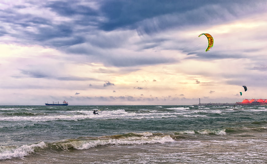 Kitesurfer riding waves under dramatic cloudy sky