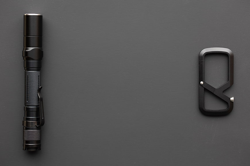 Black flashlight and carabiner on dark gray background
