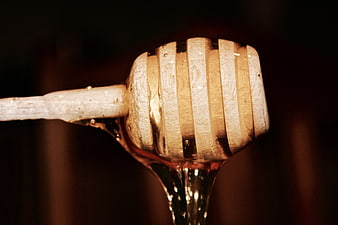 Close-up of wooden honey dipper with dripping golden honey