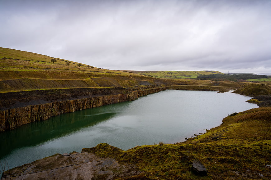Serene flooded quarry lake with steep rocky cliffs and green hills