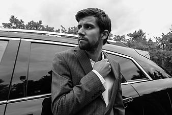 Black and white portrait of a stylish man in a suit standing by a luxury car