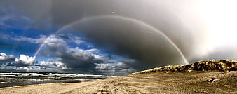 Double rainbow over sandy beach with dramatic storm clouds