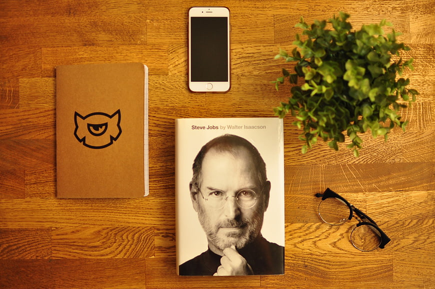 Flat lay of Steve Jobs biography, smartphone, and notebook on wooden desk
