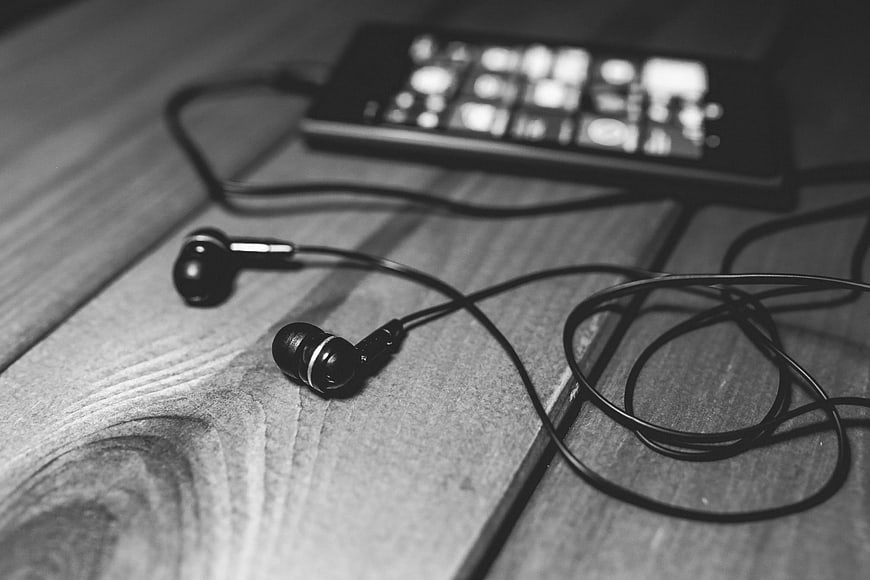 Black wired earphones and smartphone on wooden table