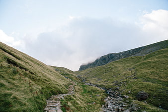 Stone path winding through green mountain valley with clouds