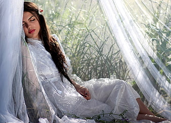 Woman in white dress and veil sitting in tall grass
