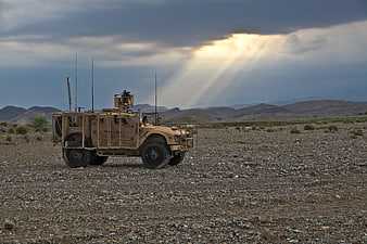 Military armored vehicle in desert landscape with dramatic storm clouds