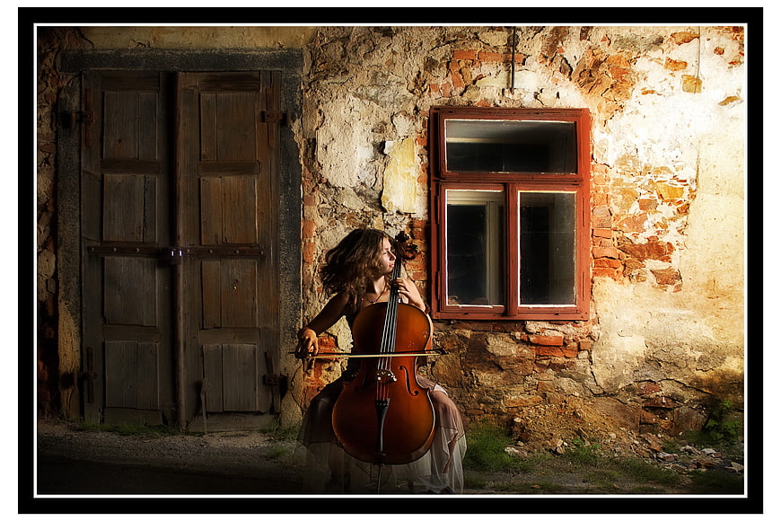 Woman playing cello in front of old rustic building