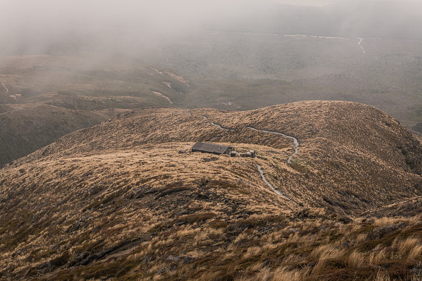 Lone cabin on misty mountain ridge with winding path