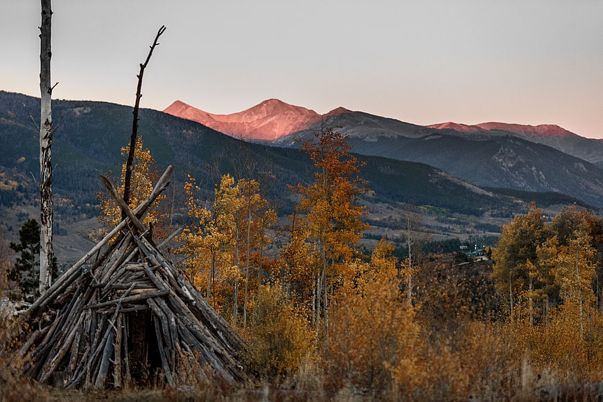 Rustic wooden shelter in autumn aspen forest with alpenglow mountains