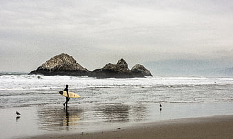 Surfer Walking on Beach with Rock Formations