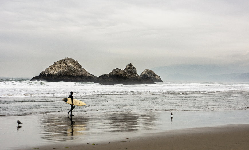 Surfer Walking on Beach with Rock Formations