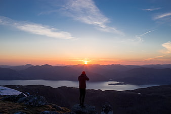 Silhouette of Hiker Photographing Mountain Sunset Over Fjord