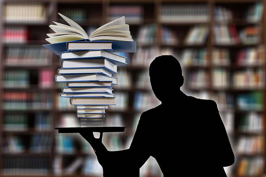 Silhouette of man holding stack of books in library