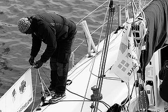 Sailor adjusting ropes on a yacht deck in black and white