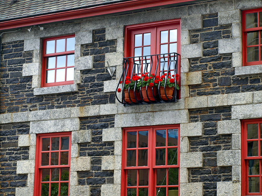 Red window frames on stone building facade with flowers